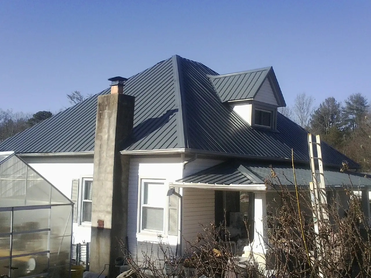 Dark blue standing seam metal roof on a white farmhouse with dormer — Slate & Tile Roof Repair by Roofing Brothers in Port Jefferson Station