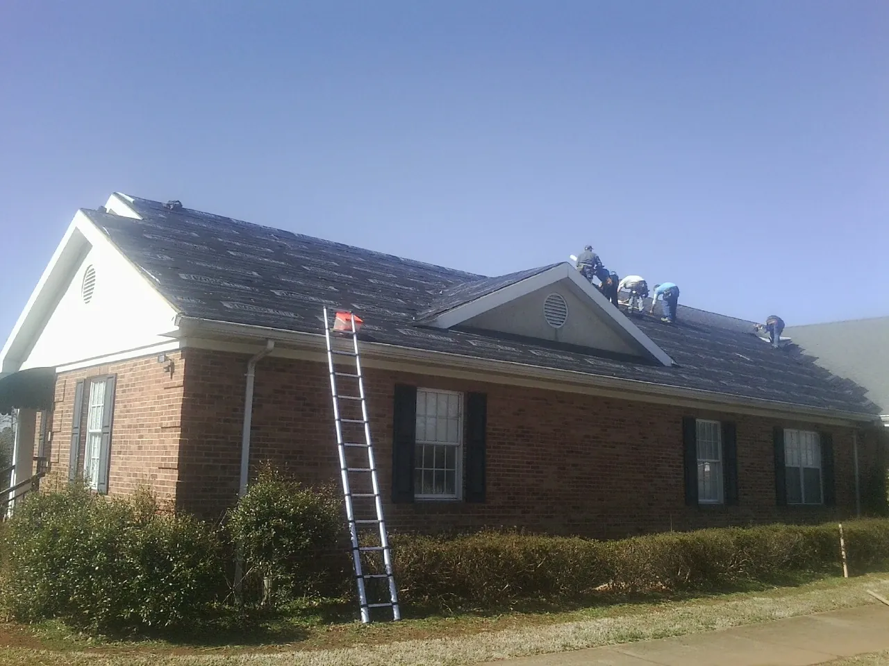 Crew tearing shingles off a brick ranch roof with a ladder set — Metal Roof Repair work by our crew in Port Jefferson Station
