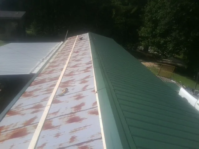 Old rusted panels beside newly installed green metal roofing — Wind Damage Roof Repair by Roofing Brothers in Port Jefferson Station