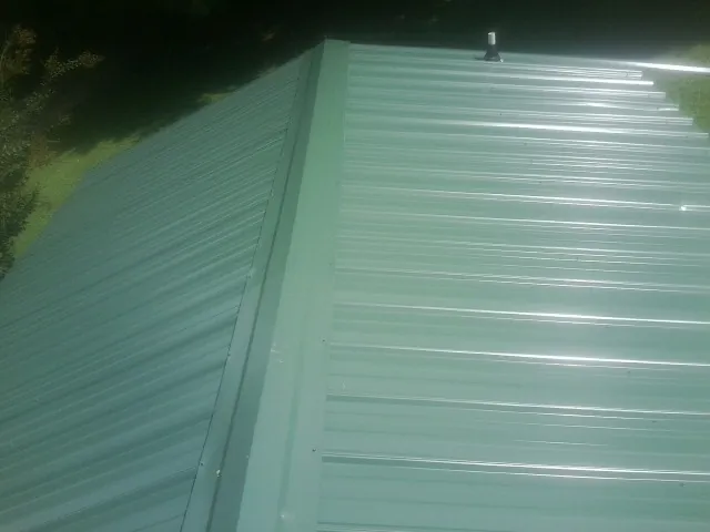 New green metal panels meeting at the ridge of a roof — Flat Roof Repair work by our crew in Port Jefferson Station