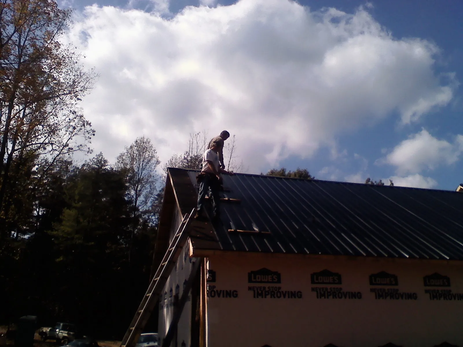 Roofer fastening dark metal panels high against a cloudy sky, from a Roof Inspection job in Port Jefferson Station