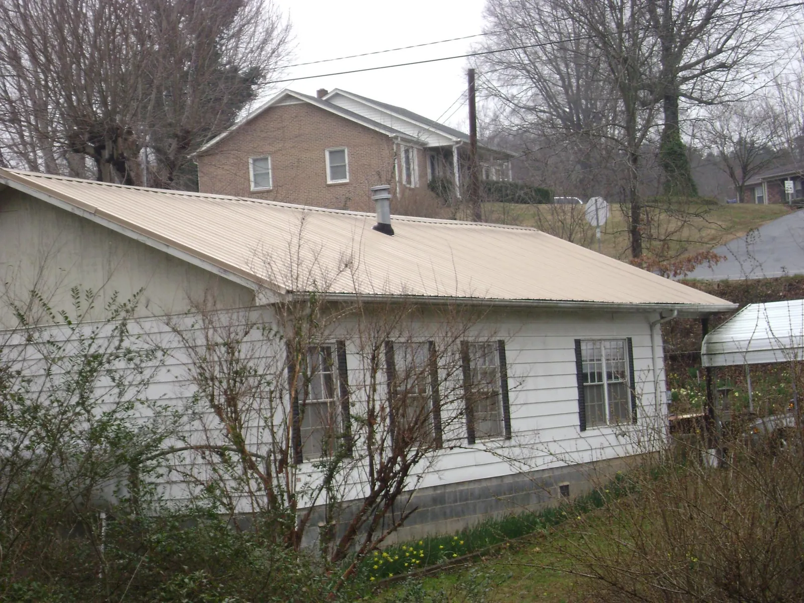 Tan metal roof on a white sided house set into a hillside — Commercial Roofing by Roofing Brothers in Port Jefferson Station
