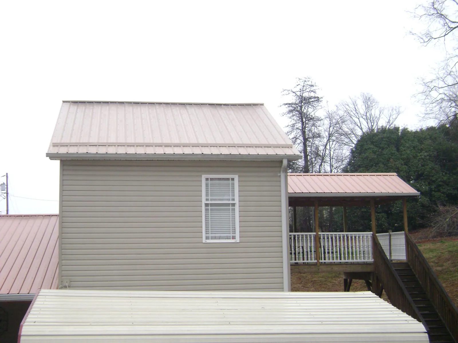 Tan metal roofs on a two story addition and attached porch, from a Roof Replacement job in Port Jefferson Station